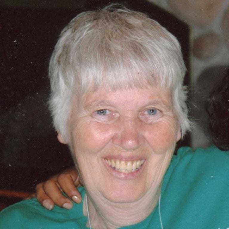A woman with short white hair smiling brightly for a headshot picture while wearing a green blouse.