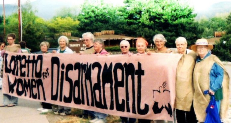 Loretto Community members wearing sackcloth stand by the sidewalk with a banner that reads "Loretto Women for Disarmament."
