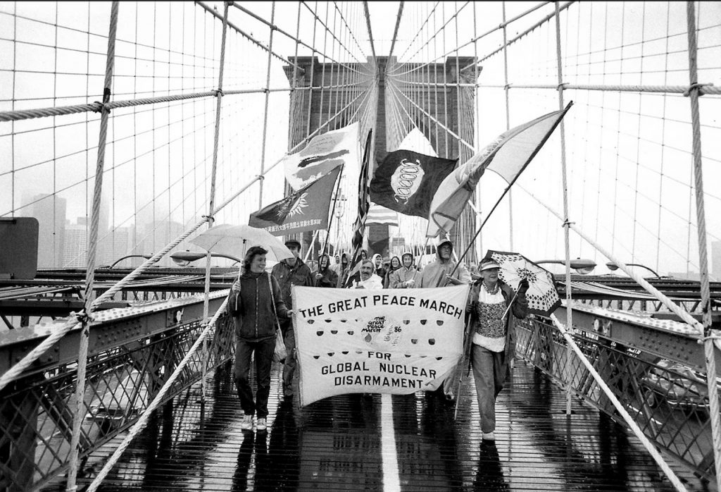Marchers carry a banner as they cross a pedestrian bridge. The banner reads "The Great Peace March for Global Nuclear Disarmament."