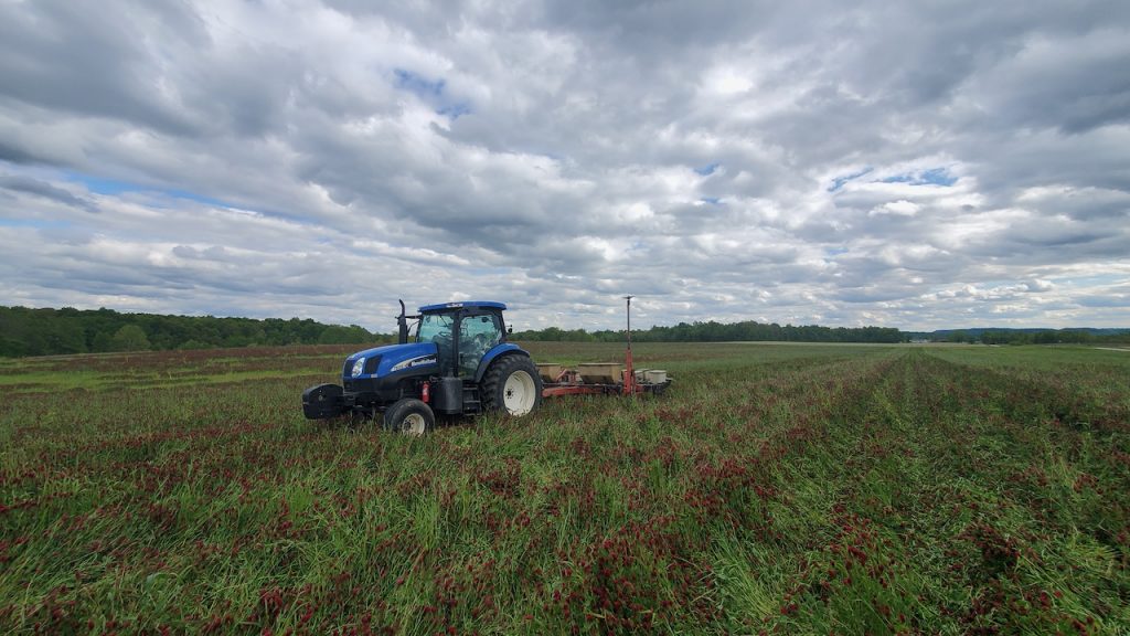 A tractor sits in the middle of a field with dramatic clouds above.