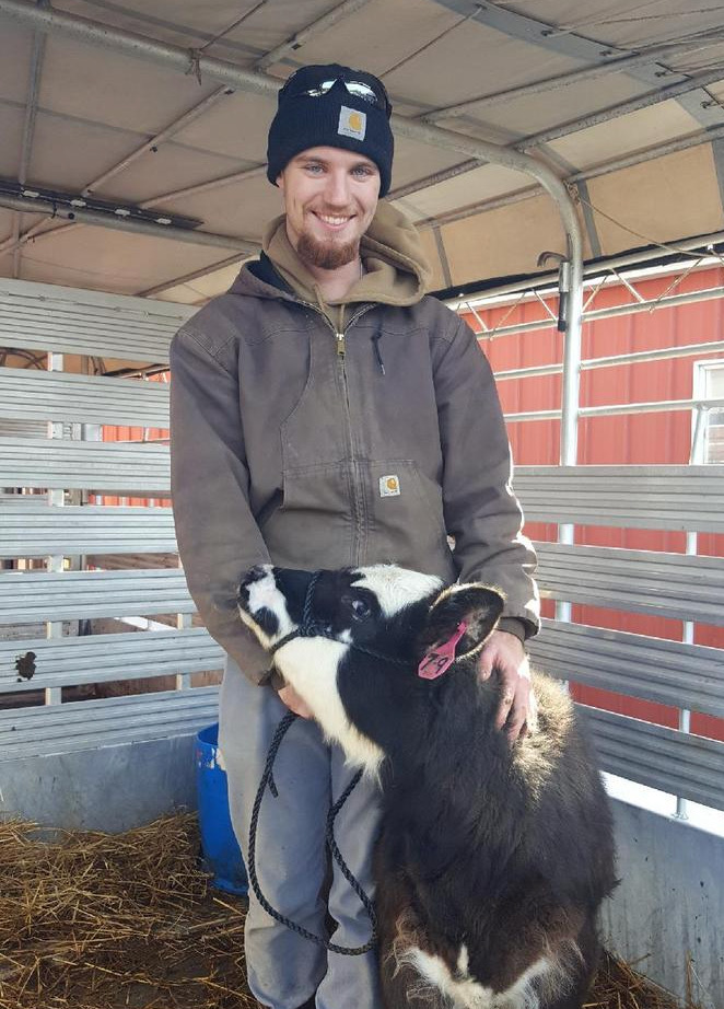 A smiling man holds the head of a black and white calf.