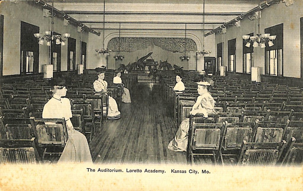 Historical photo of several women sitting in chairs in an auditorium.