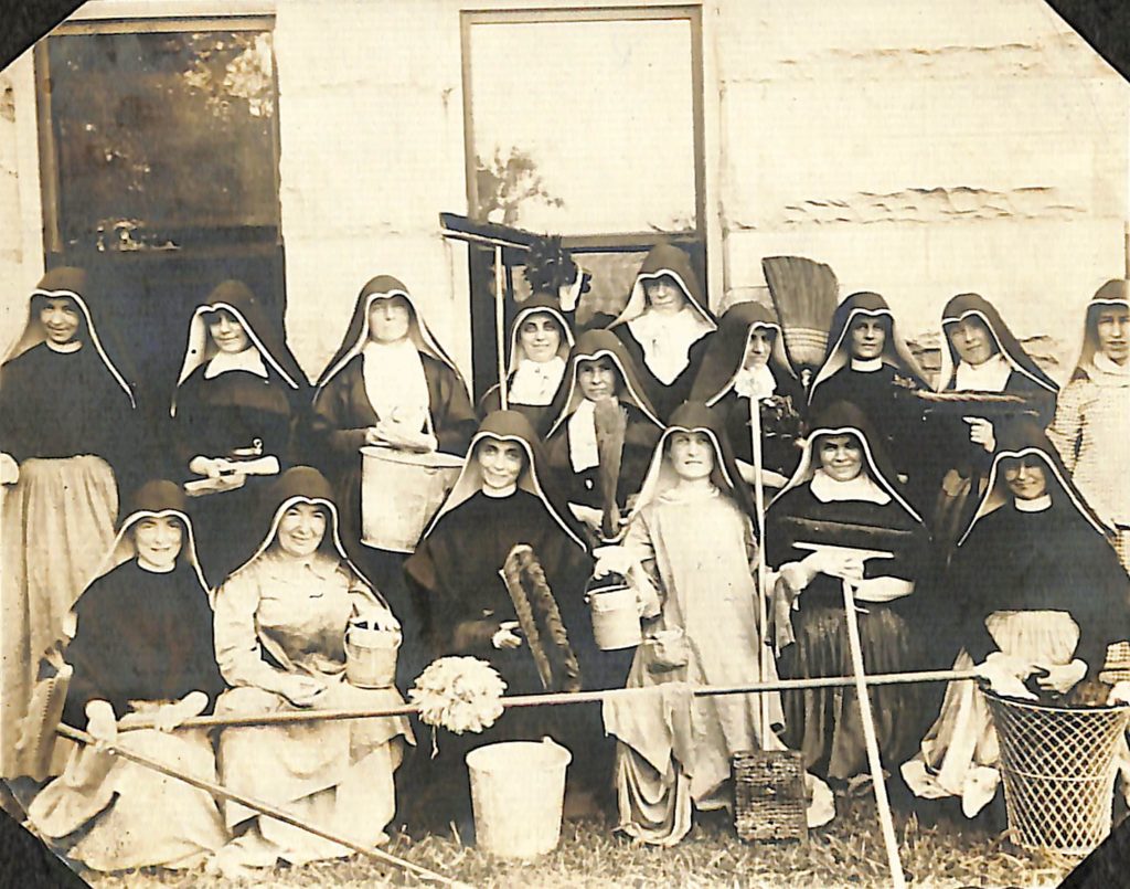 Historical photo of group of Sisters of Loretto sitting outside with cleaning supplies and implements