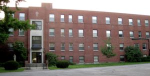 Long, four story brick building with a cross above the entrance.