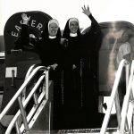 Archival photo of two sisters in habit waving from the door of a plane.