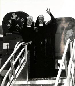 Archival photo of two sisters in habit waving from the door of a plane.