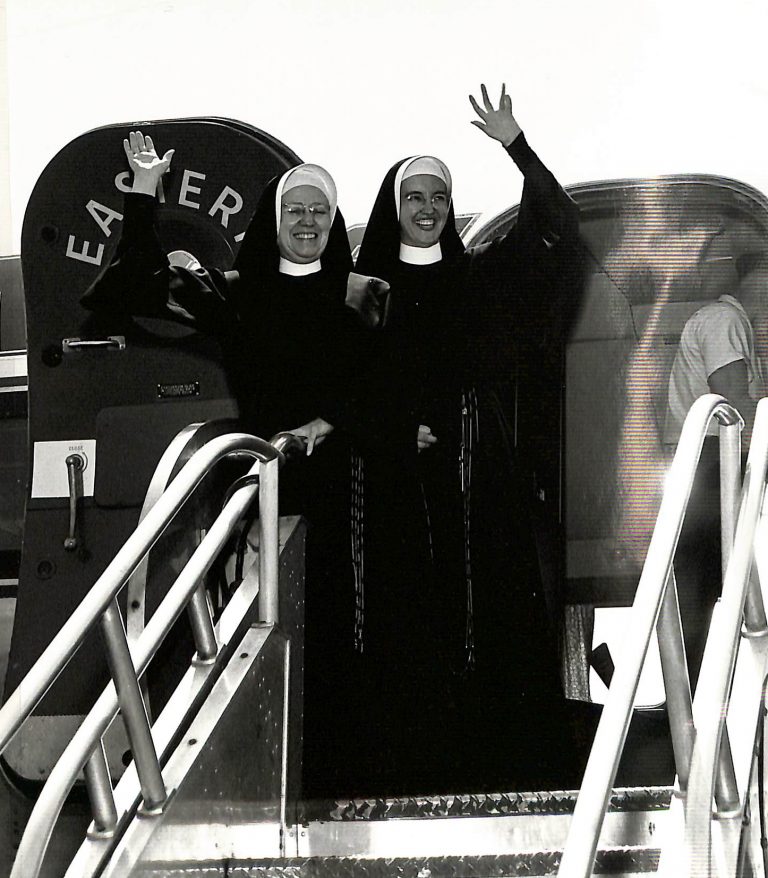 Archival photo of two sisters in habit waving from the door of a plane.