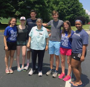 A group of high school students stand around a sister on a warm, sunny day.