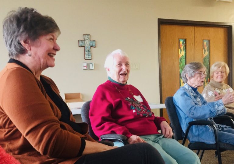 Women sitting in meeting chairs talk and laugh together.