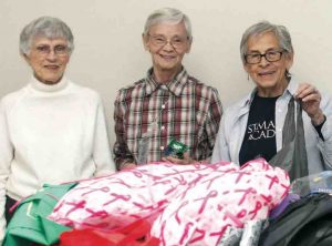 Three women stand behind boxes of donated clothing.