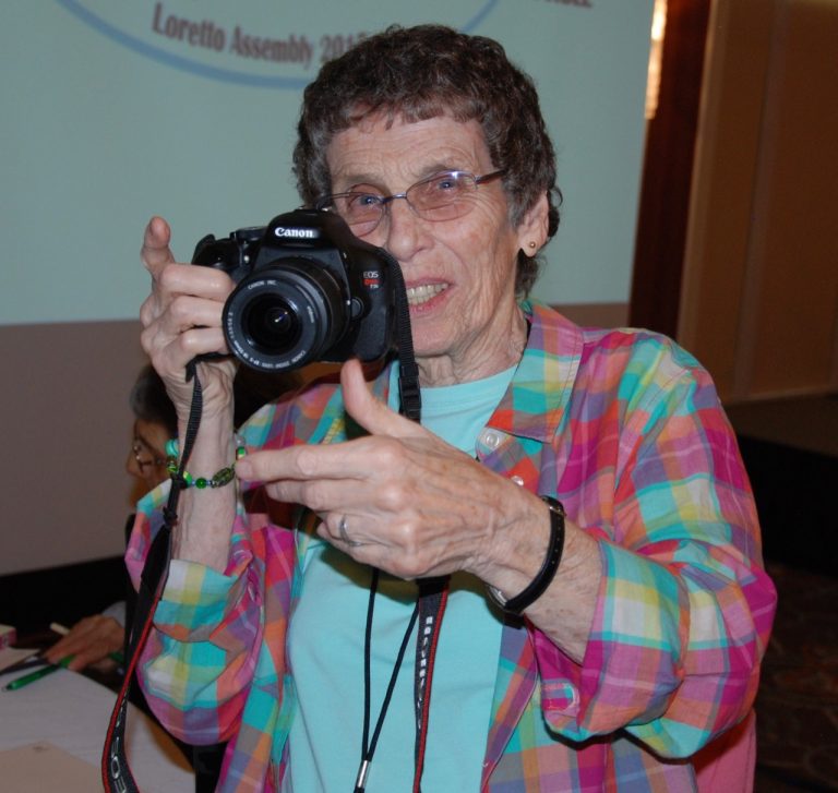 A woman smiles from behind her camera.