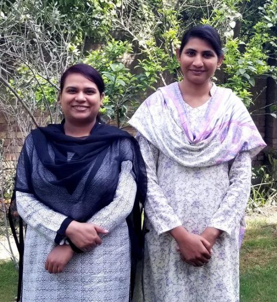 Two women in traditional Pakistani attire stand shoulder to shoulder.