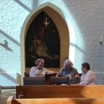 Three women sit in a church, conversing.