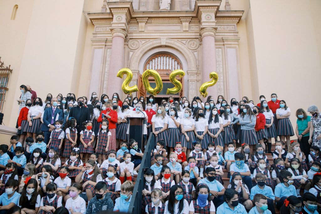 A crowd of students in school uniforms stand on the steps with balloons reading 2022