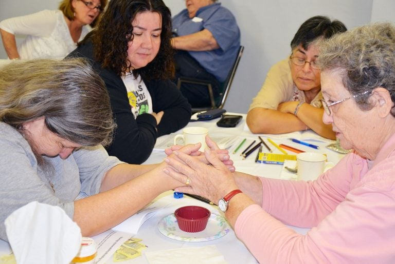 Two women hold hands in prayer, while others reflect