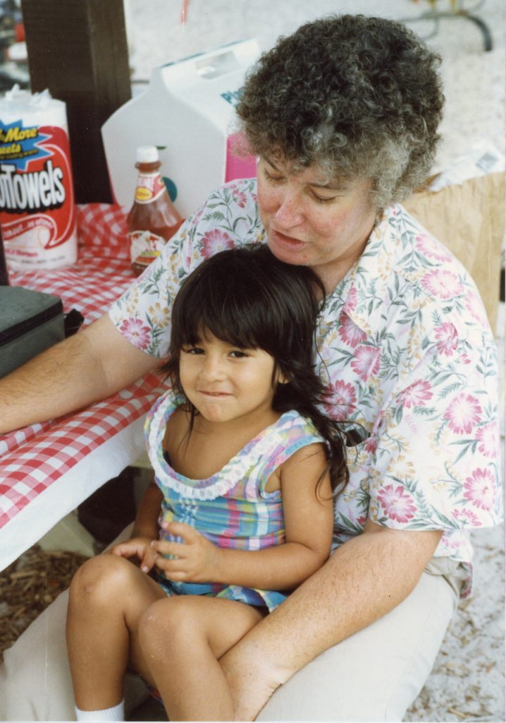 A woman sits with a small girl on her lap at a picnic table