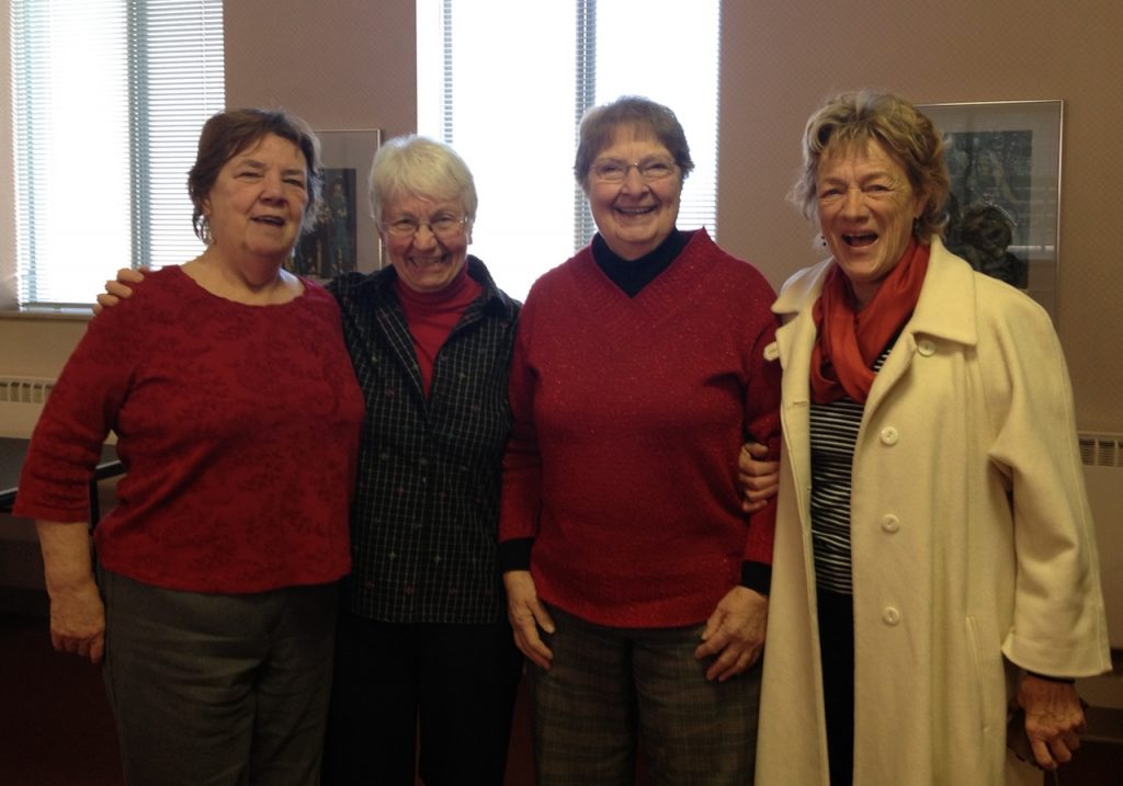 Four women stand arm and arm, smiling and laughing for the camera