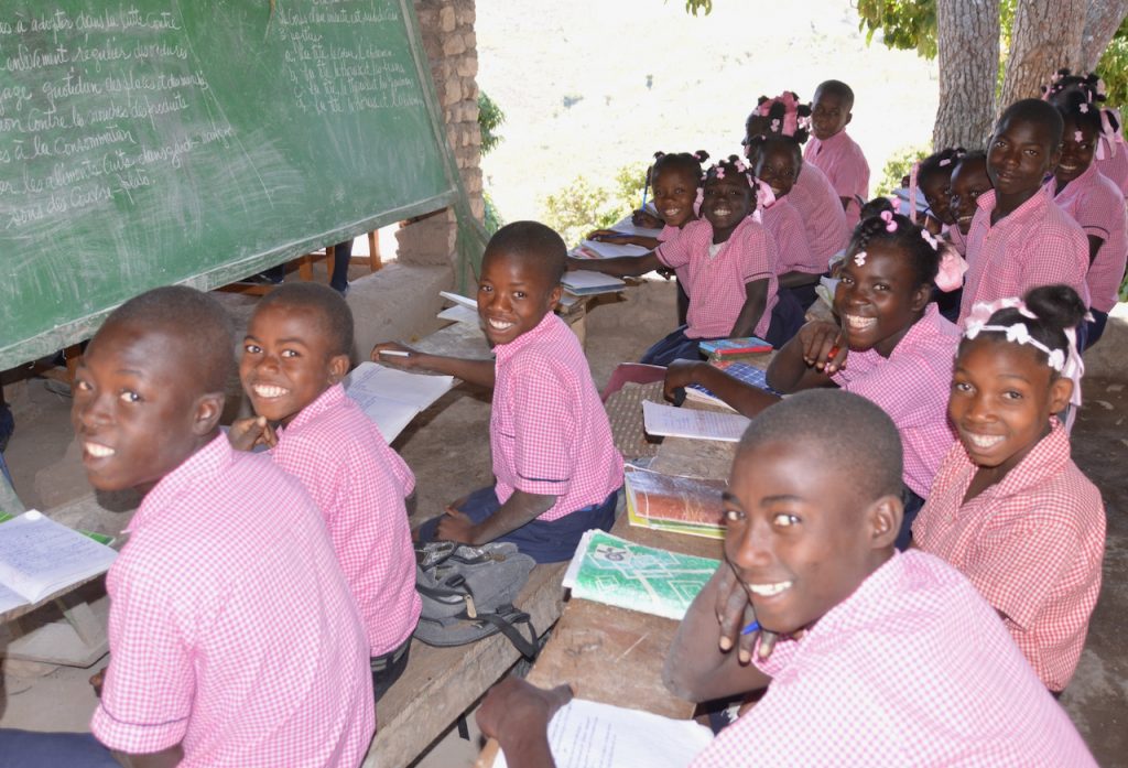 Haitian students in school uniforms sit in front of the chalkboard.