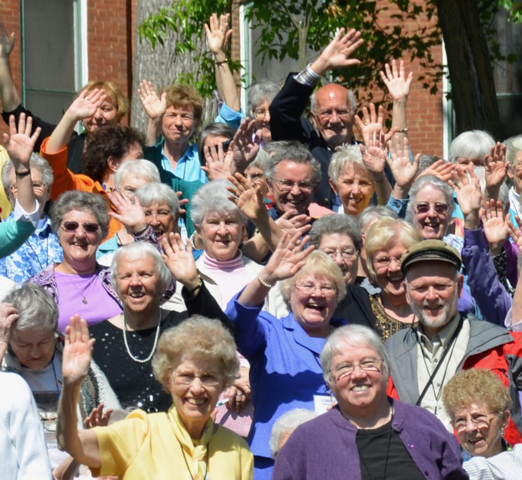 A crowd of smiling people waves for the camera