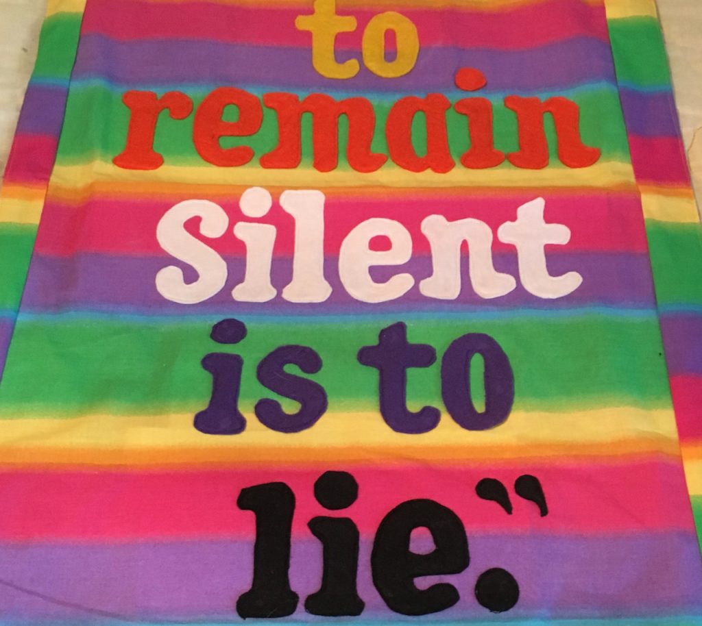 Colorful banner featuring these words from Unamuno's quote "to remain silent is to lie." Banner by Robert Strobridge CoL