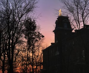 A Christmas star on top of a building is profiled against the pinks and purples of the sky at sunset.