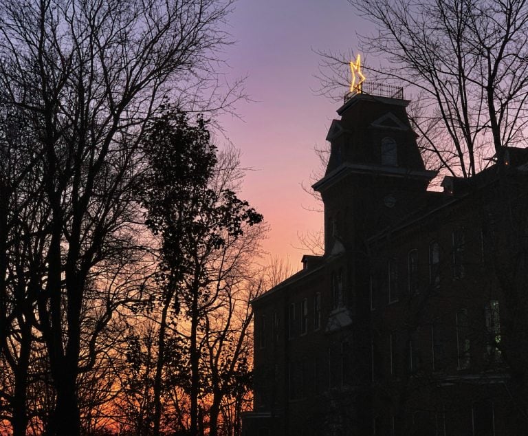A Christmas star on top of a building is profiled against the pinks and purples of the sky at sunset.