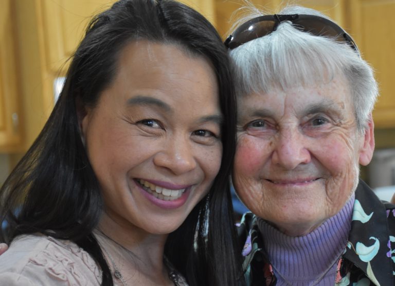 Two women, one Vietnamese and one White, embrace and smile for the camera.