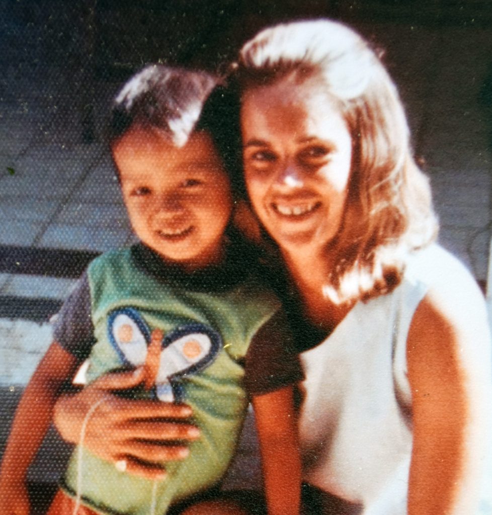 A young boy sits on the knee of a smiling woman.