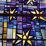 A stained glass window shines with golden stars and a blue and purple background