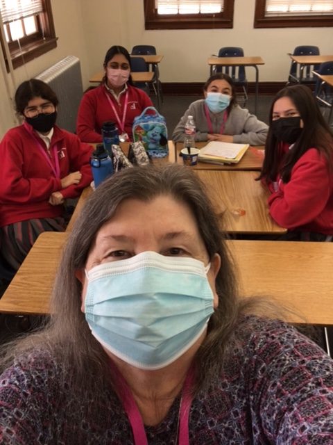Woman in mask takes a selfie with students in school uniforms.