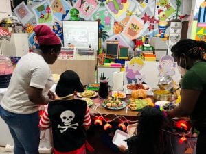 Two Black women assist two children at a buffet table.