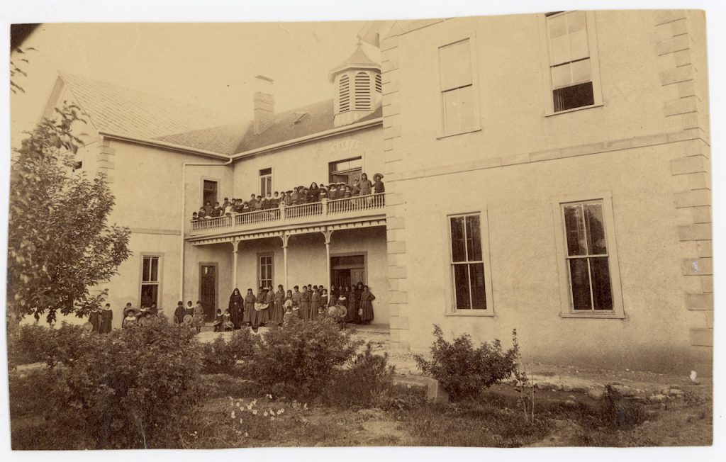 Archival photo of students and sisters standing on the porch and balcony of a large building.