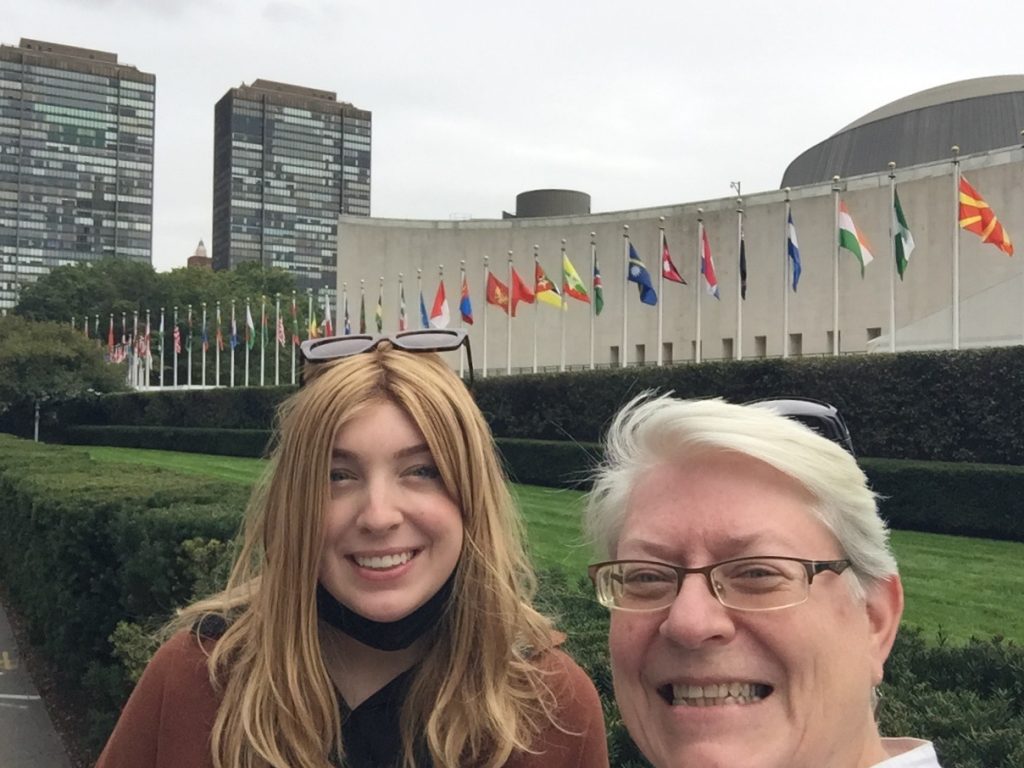 Two women smile in a selfie, with the flags of nations in the background.