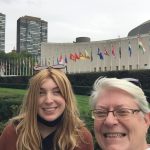 Two women smile in a selfie, with the flags of nations in the background.