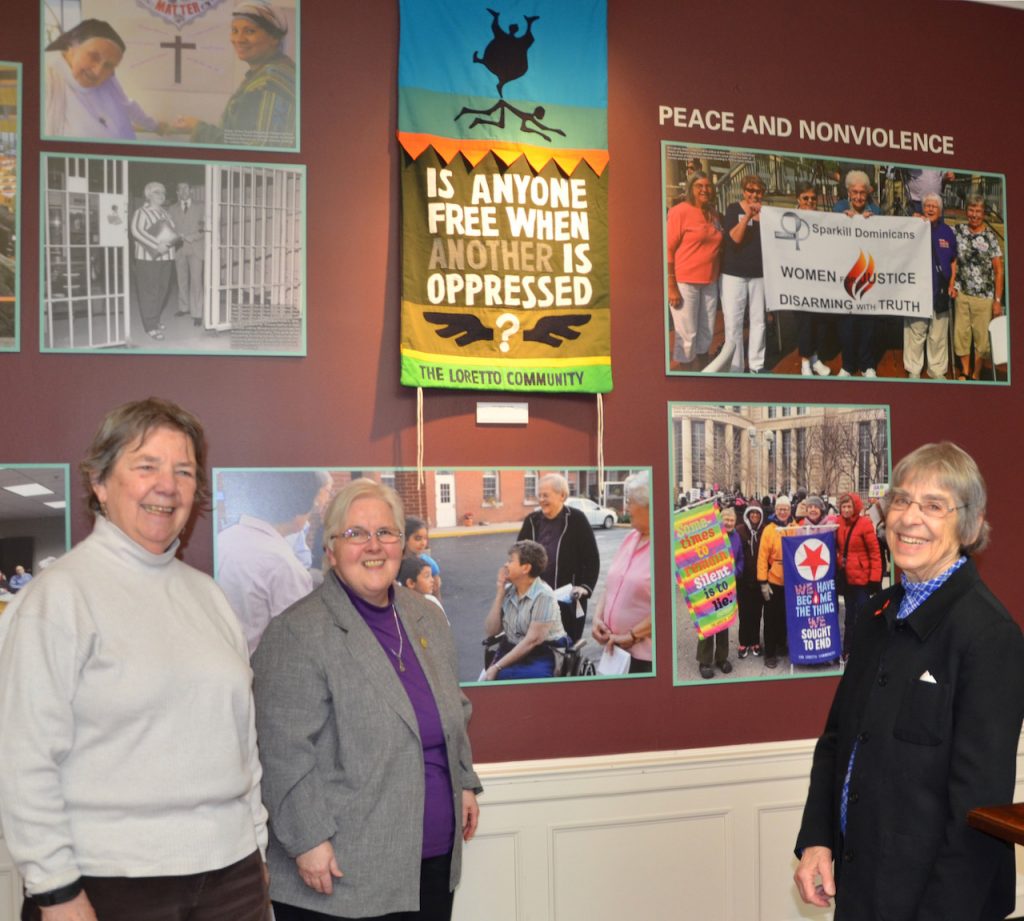 Three women smile in front of a wall of historical photos