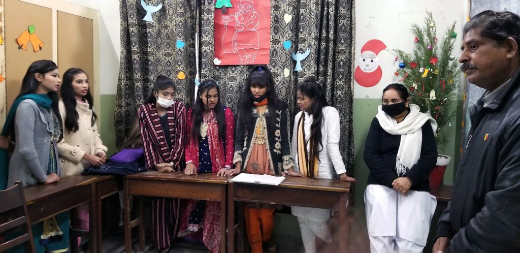 Young Pakistani women stand at their desks during a Christmas performance.