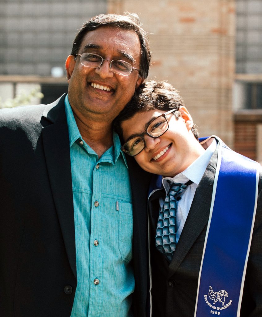 A boy in a graduation gown stands with his father.