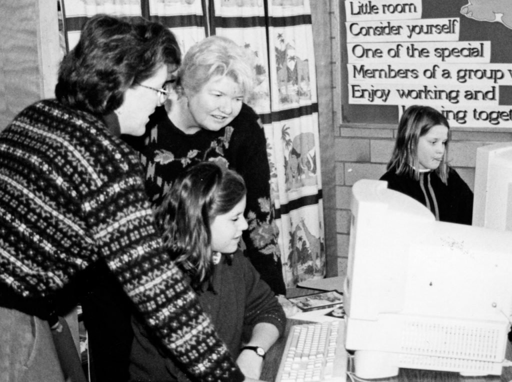 Black-and-white photo of two women looking over a female student's shoulder at her computer screen.