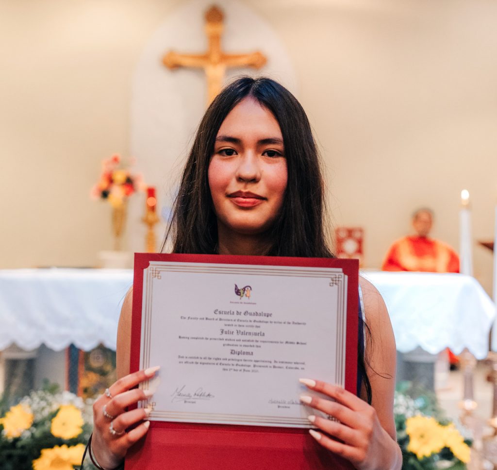 A young woman holds up her diploma.