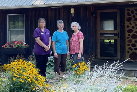 Renee Edelen, Susan Classen and JoAnn Gates stand in front of a rustic building amidst bright flowers.