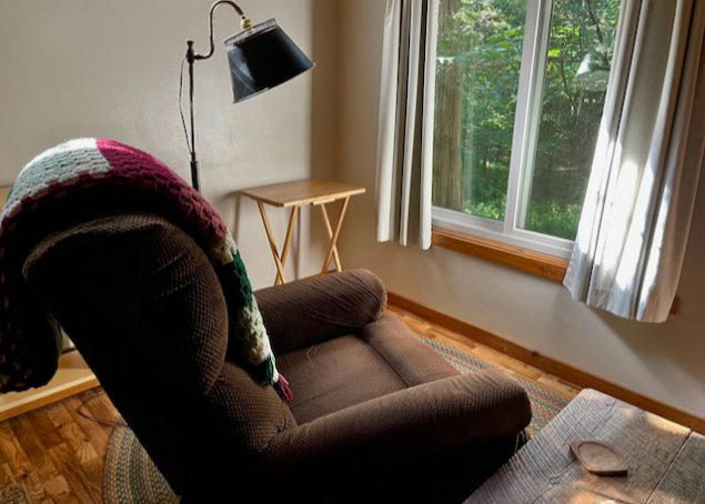 An easy chair faces a window with a view of the forest.