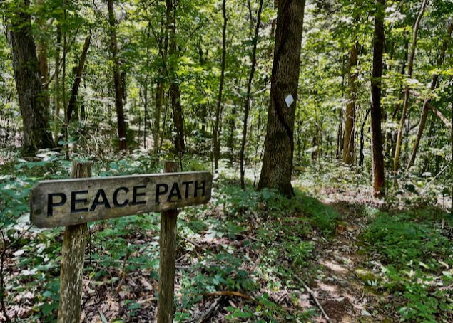 Carved wooden sign reads next to a trail into the woods reads "Peace Path."