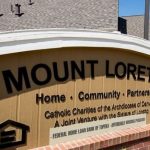 Sign outside building reads "Mount Loretto: Home. Community. Partnership" Subheading: Catholic Charities of the Archdiocese of Denver. A Joint Venture with the Sisters of Loretto.