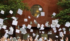 Hands toss white graduation caps with green tassels into the air.