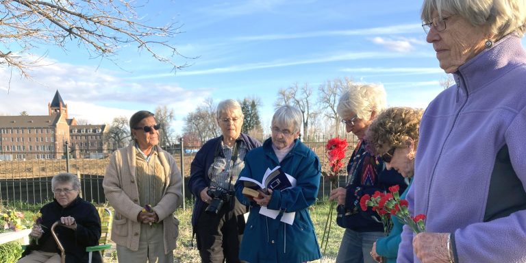 A group of people holding flowers gather outside in prayer on a spring evening.