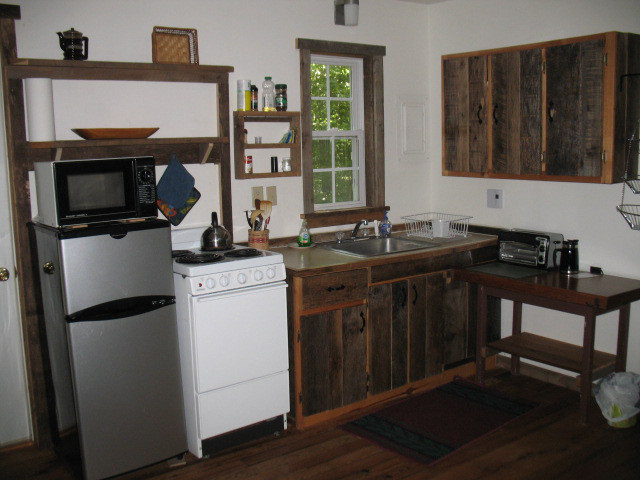 A studio kitchen with small refrigerator, stove/oven, sink with counter and a few cupboards.