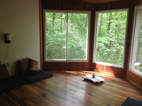 Ceiling to floor windows form a bay on one side of a minimally furnished room.