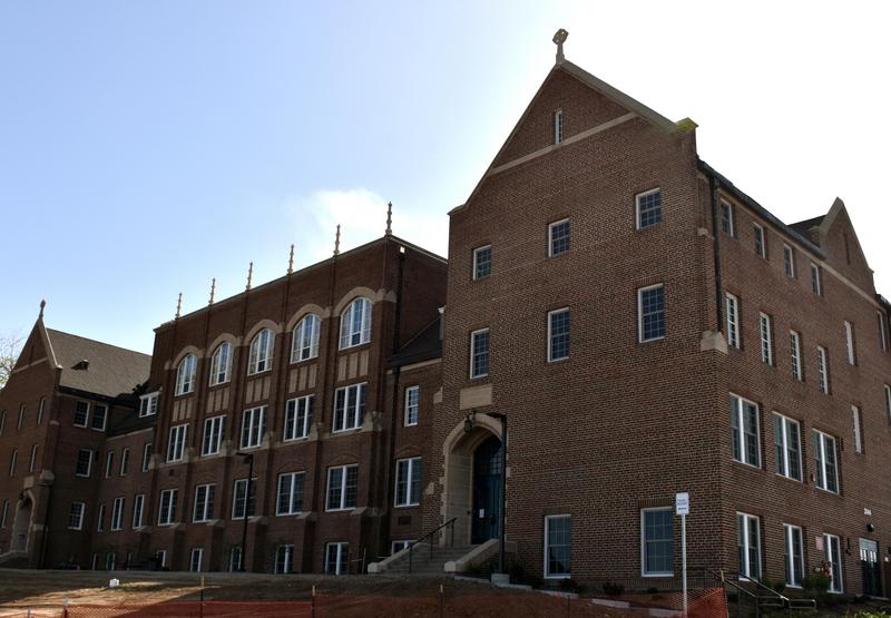 Photo of a large, four-storey brick building with a center hub and two gabled wings.