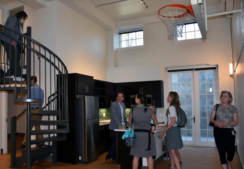 People gather in a refurbished apartment room with a spiral staircase and basketball hoop. 