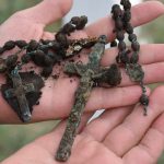 A rusted and dirt crusted rosary is displayed in outstretched hands.